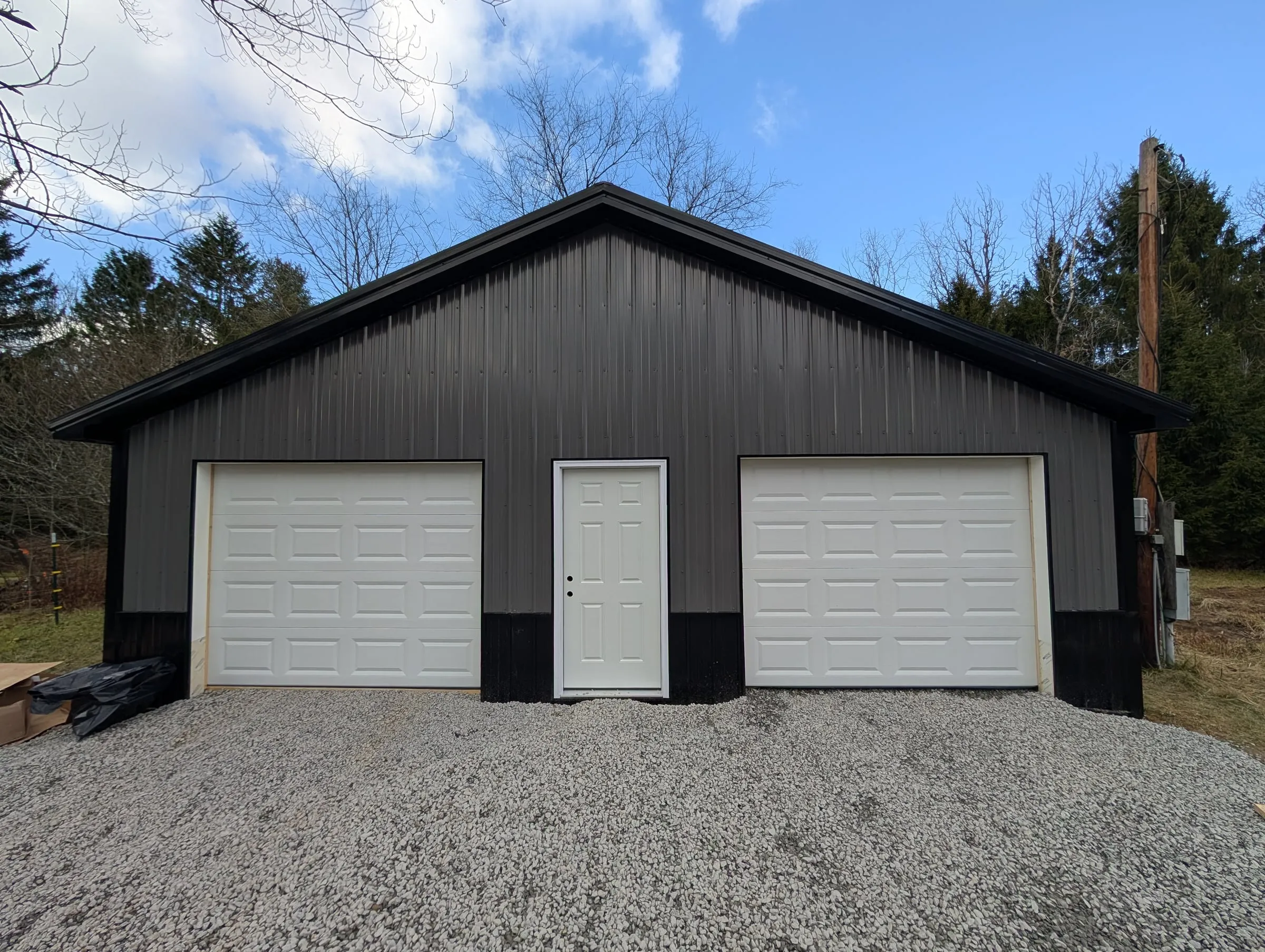 Finished two-bay garage with dark gray steel siding, black wainscot and trim, two white overhead doors and a white walk-in door